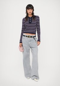 Námornícky a biele pruhované tričko s dlhým rukávom, golierom a gombíkmi, doplnené svetlomodrými širokými džínsami a ružovou kabelkou. Biele špicaté topánky.