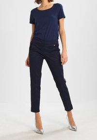 Mörkblå T-shirt med korta ärmar, kombinerad med slim-fit mörkblå byxor med sidostrekar, bärs med silverfärgade högklackade skor.