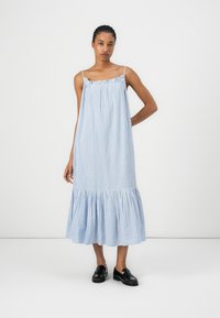 Modrá a biela pruhovaná bavlnená šaty s voľným strihom, naberaným spodným lemom a tenkými ramienkami. Nosia sa s čiernymi topánkami.