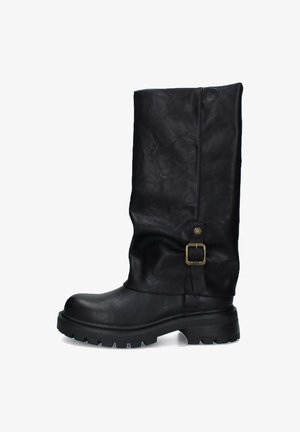 Stivale alto in pelle nera con suola chunky e fibbia decorativa in ottone sul lato, su sfondo bianco.