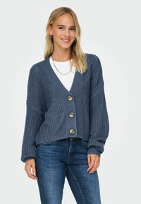 Stickad kofta i marinblått med V-ringning, långa ärmar och fyra stora knappar. Tillverkad av en texturerad tyg med en lös passform.