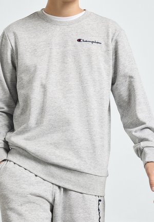 Homme portant un sweat-shirt Champion gris clair et un pantalon de survêtement assorti avec broderie du logo sur la poitrine et le pantalon.