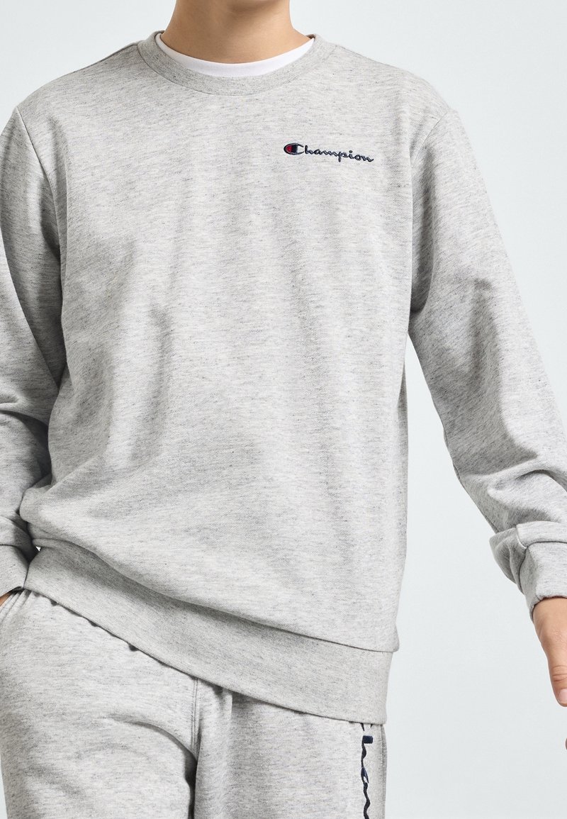 Homme portant un sweat-shirt Champion gris clair et un pantalon de survêtement assorti avec broderie du logo sur la poitrine et le pantalon.