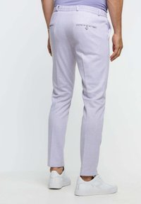 Pantalones ajustados de color púrpura claro con corte entallado, que cuentan con dos bolsillos traseros y una textura sutil, combinados con zapatillas blancas.