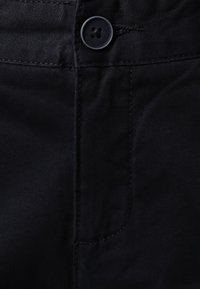 Czarna denimbrowa tkanina o subtelnym połysku, z ozdobnym guzikiem i detalami przeszywania wzdłuż szwów i kieszeni.