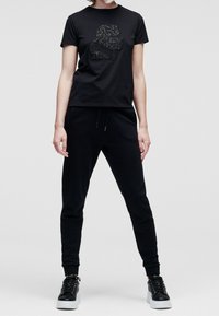 Svart t-shirt med en strukturerad, glittrande grafisk design som föreställer en profil. Kombinerad med svarta joggerbyxor och stiliga svarta sneakers.