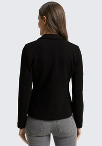 Blazer nero in tessuto texturizzato con una vestibilità strutturata, colletto a risvolto e maniche lunghe. Presenta dettagli di cucitura e una fodera interna liscia.