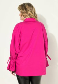 Fuchsia-bluse mit langen Ärmeln, Kragen und Schleifen an den Manschetten. Glatte Textur, hüftlanges Design, minimalistischer Stil.