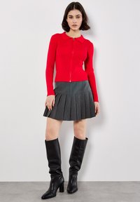 Czerwony, prążkowany, długi rękaw, zapinany top w połączeniu z plisowaną, szaro-paskowaną spódnicą i czarnymi, wysokimi na kolana botkami, z dopasowaną sylwetką.