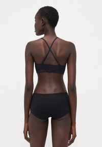 Mustat bralette -toppi, jossa on ristikkäiset hihnat, ja siihen sopivat mustat shortsit. Pehmeä kangas, istuva muotoilu, minimisaumat ja ei näkyviä kuvioita.