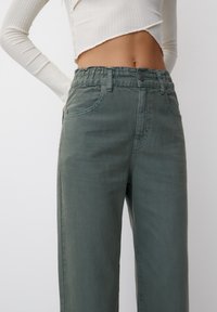 Pantalon large couleur vert olive avec une taille élastique, des poches avant et une texture subtile. Assorti à un haut court à manches longues.