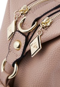 Borse in pelle rosa chiaro, con una vista ravvicinata che mostra doppie cerniere, hardware dorato e charm decorativi a forma di diamante e con il logo.