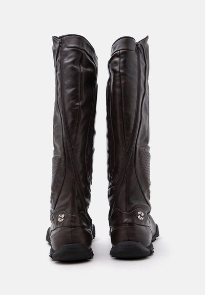Paire de bottes hautes en cuir brun foncé vues de dos, avec des fermetures éclair sur les côtés et des semelles à motif antidérapant.