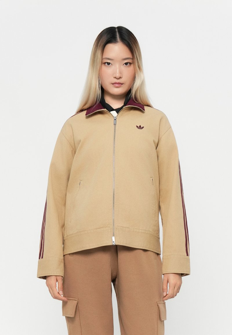 Beige jacket with a maroon collar, zip closure, and three maroon stripes along the sleeves. Features a small logo on the chest.