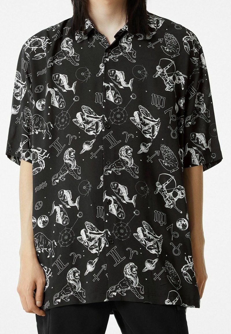 Camisa negra de manga corta con botones, con símbolos astrológicos blancos y gráficos de animales, confeccionada en una tela suave y con un corte holgado.