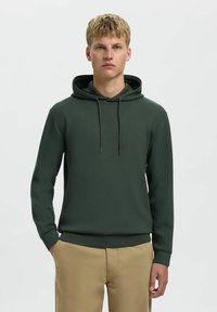 Felpa verde scuro realizzata in tessuto morbido, con cappuccio regolabile, maniche lunghe e polsini a coste, dal taglio rilassato.