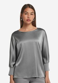 Blusa in raso grigio con maniche a tre quarti, scollatura rotonda e texture liscia. Presenta una vestibilità morbida e una caduta lieve.