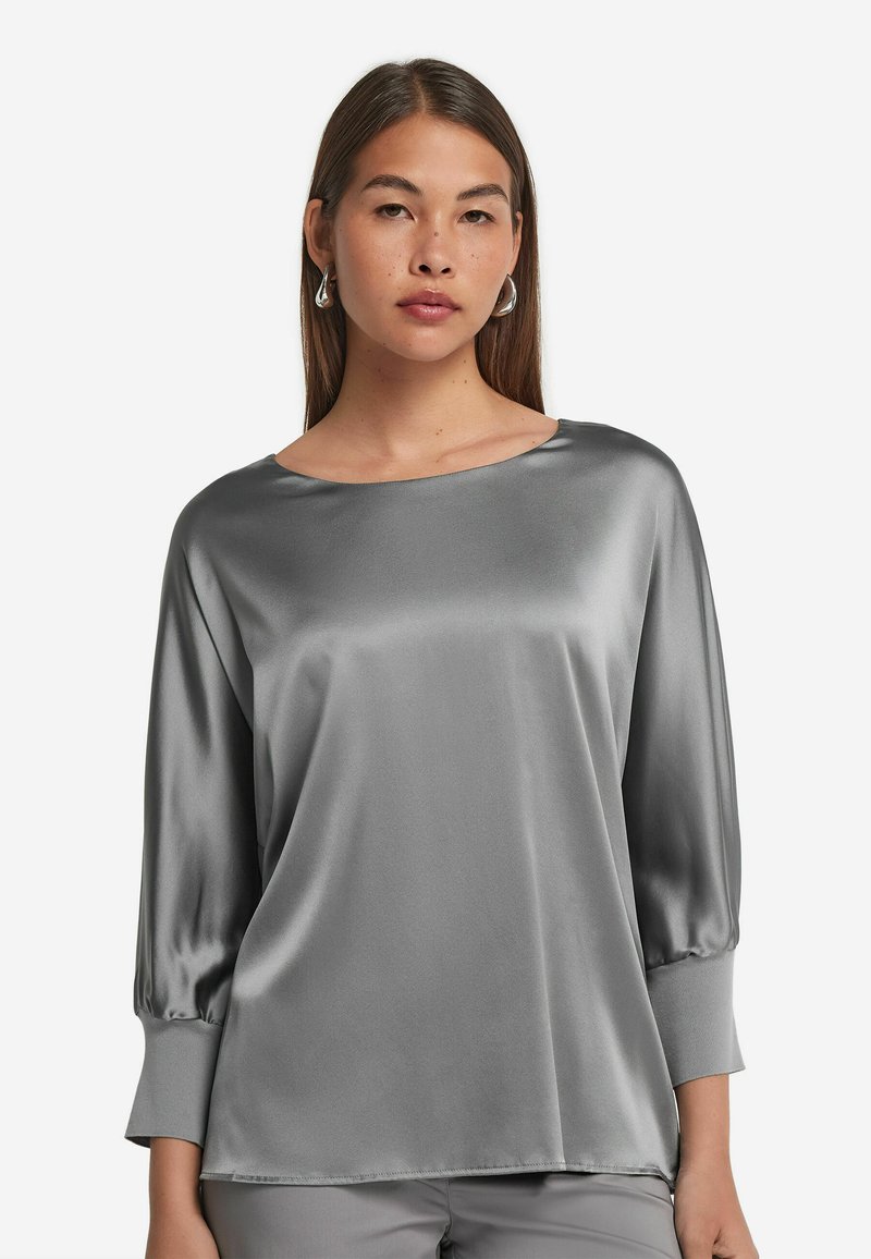 Blusa in raso grigio con maniche a tre quarti, scollatura rotonda e texture liscia. Presenta una vestibilità morbida e una caduta lieve.