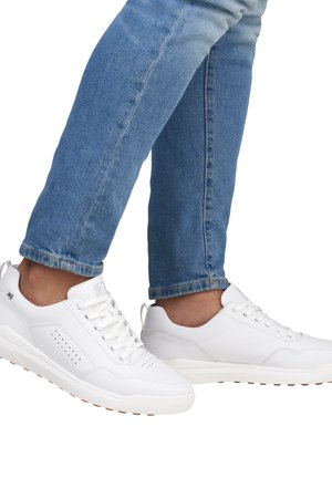 Hvide sneakers med en glat læderoverdel, rund tå og perforerede detaljer; parret med lyseblå denimjeans, som er let slidte ved anklerne.