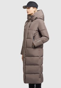 Long, padded coat made of smooth, taupe fabric with a hood, side pockets, and zippers. Features a vertical quilted design.