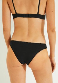 Zwarte katoenen bikini met een gladde textuur, voorzien van een low-rise snit en dunne bandjes, geaccentueerd met een minimalistisch logo op de tailleband.