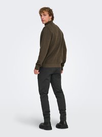 Pull-over vert olive avec un col montant, en matière texturée. Associé à un pantalon slim gris foncé et des chaussures noires.