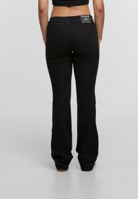 Pantalones vaqueros negros acampanados de denim. Cuenta con dos bolsillos traseros, acentos de costura y una etiqueta en la cintura. Ajuste entallado desde la cintura hasta la rodilla.