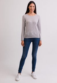 Maglione grigio chiaro a maniche lunghe con scollatura rotonda, abbinato a jeans skinny blu scuro e sneakers bianche. Texture morbida, vestibilità casual.