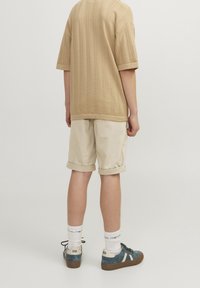 Beige textuur trui met korte mouwen, lichtbeige opgerolde shorts, blauwe sneakers met witte accenten en witte sokken.