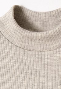 Maglione lavorato a maglia con una texture a coste, di colore beige chiaro e con un design a collo alto. Il tessuto appare morbido e leggermente elastico.