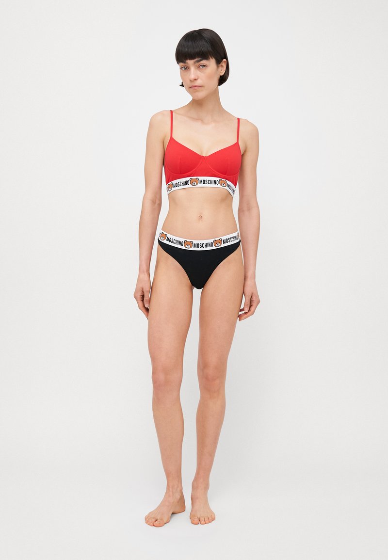 Bralette rembourré rouge avec fines bretelles et bas de bikini noir. La bande présente un logo Moschino avec un graphique d'ours. Le matériau semble lisse.