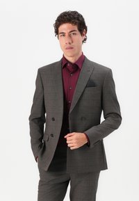 Grey checkered suit with a double-breasted design, black buttons, and a black pocket square. Worn over a burgundy shirt. Smooth texture.