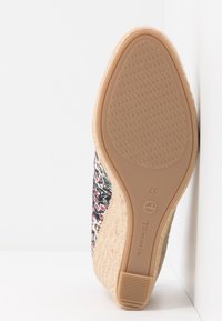 Semelle d’une chaussure compensée avec dessus en tissu floral, semelle extérieure en caoutchouc beige texturé, nom de marque Tamaris et taille 37 visible sur la semelle.