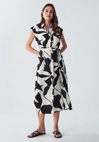 Abito a righe in bianco e nero con colletto a camicia, maniche corte, cintura in vita e tasche, realizzato in un tessuto leggero, design a lunghezza media.