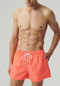 Męskie kąpielówki w kolorze koralowym, elastyczny pas z białym sznurkiem, gładki materiał, długość powyżej kolan, kieszenie boczne, minimalistyczny design.