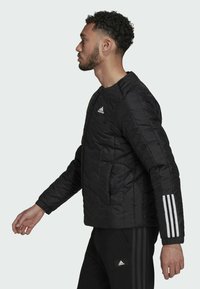 Zwarte pufferjack met een gestikte textuur, voorzien van een wit Adidas-logo en drie strepen op de mouwen, geplaatst tegen een lichte achtergrond.