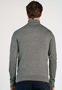 Grau gestrickter Rollkragenpullover mit langen Ärmeln, gerippten Bündchen und Saum. Hat eine weiche Textur und ein figurbetontes Design. Keine sichtbaren Logos.