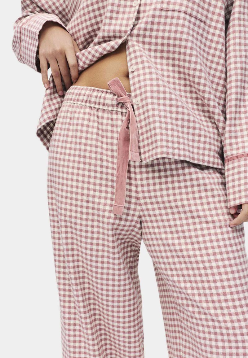 Ensemble de pyjama en vichy en coton doux avec des carreaux roses et blancs. Taille à cordon de serrage et haut à boutons avec des manches longues.