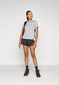 Grå kortermet t-skjorte med logo, kombinert med svarte shorts. Modellen har på seg svarte støvler og bærer en ryggsekk. Enkelt og funksjonelt design.