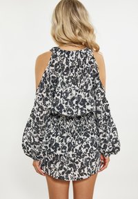 Abito a stampa floreale con design a spalle scoperte, caratterizzato da motivi in bianco e nero, maniche a campana e vita arricciata. Tessuto di trama liscia.