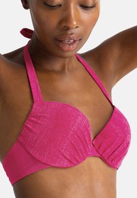 Rožinis tekstūruotas bikini viršus su paminkštintais puodeliais, kaklo nusirišimu ir susiraukšlėjimais šonuose formai ir atramai. Lygi paviršiaus apdaila.