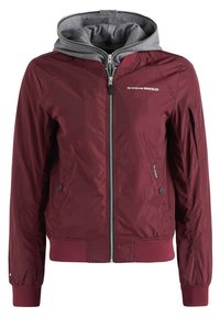 Vínová bomber bunda se šedou kapucí, zipem na přední straně, elastickými manžetami a lemem, vybavená bočními kapsami a logem na hrudi. Lehký materiál.