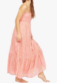 Robe maxi florale rose avec fines bretelles, corsage froncé et jupe à volants. Tissu léger, design fluide, ourlet à mi-mollet.