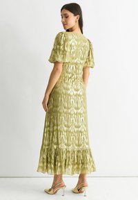 Long green dress with puffed sleeves, textured fabric featuring a subtle pattern, and a ruffled hem, paired with beige heeled sandals.