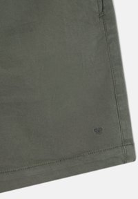 Bermudas de color verde oliva hechas de una tela suave, con un sutil logo de tijeras en el dobladillo, con costuras cuidadas y un corte relajado.