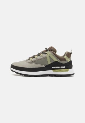 Zapatilla Timberland de caña baja en beige, verde oliva y negro con suela blanca y logo lateral, con cierre de cordones y suela exterior resistente.