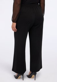 Zwarte broek met wijde pijpen van zachte stof, met een elastische tailleband en een subtiele stippenpatroon, gecombineerd met zwarte hoge hakken.