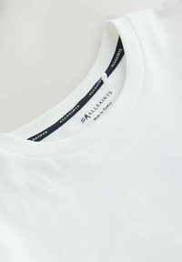 Bílé tričko s kulatým výstřihem, se štítkem značky "ALLSAINTS" a nápisem "Made in Turkey" uvnitř límce.