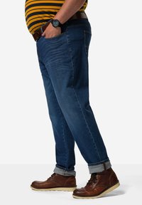 Jeans de mezclilla azul con un corte relajado, que presentan dobladillos acampanados y un ligero desgaste, combinados con botas de cuero marrón y un cinturón marrón.