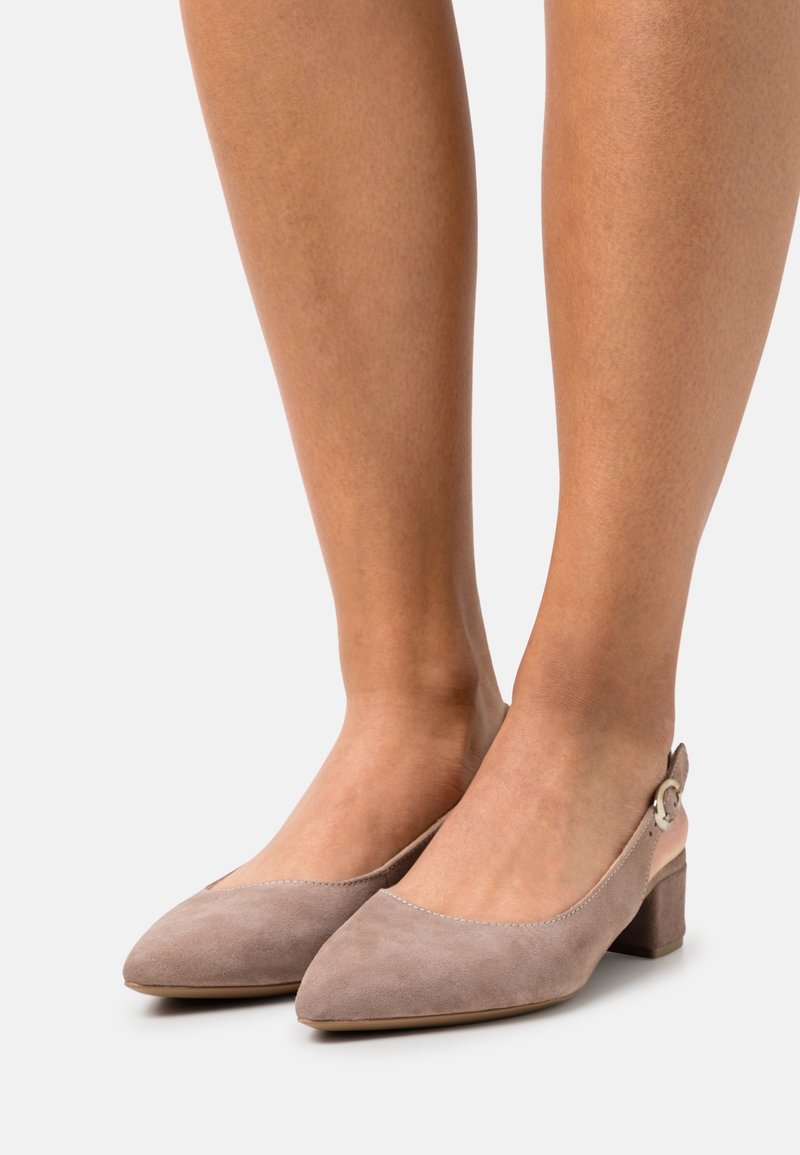 Dei tacchi slingback beige in suede con punta affusolata, tacco cubano basso e dettagli con fibbia circolare alla caviglia. Texture liscia e design elegante.